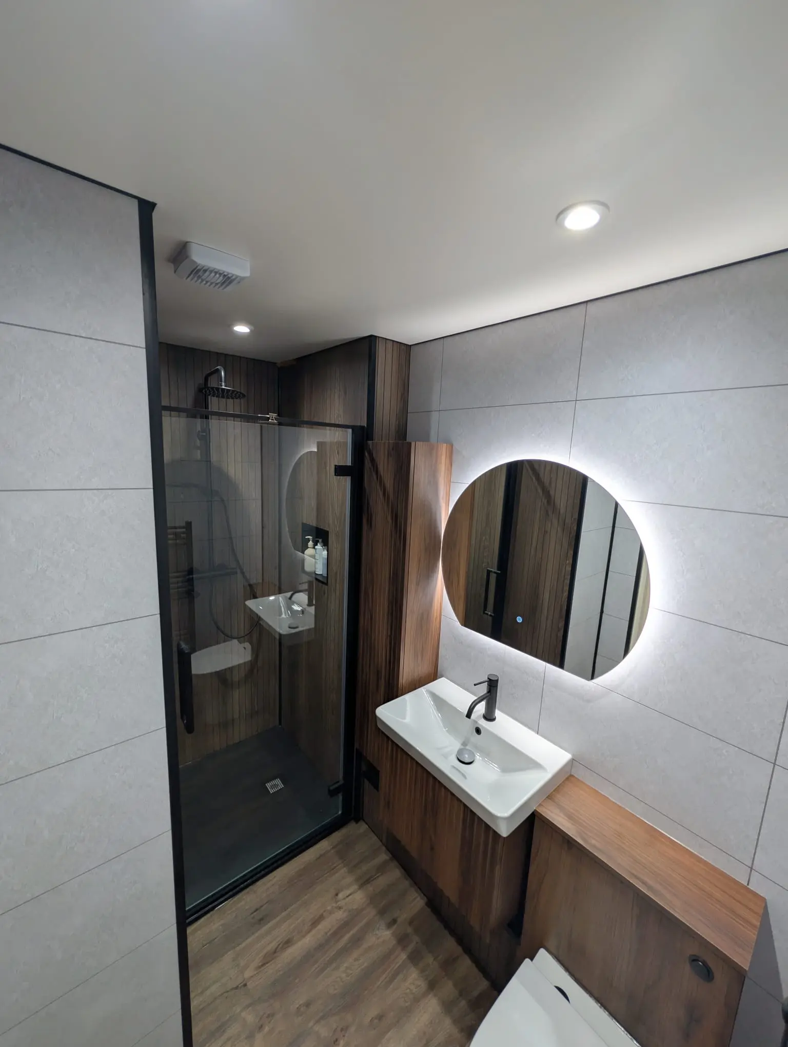 En-suite with walnut wet wall panels, black framed shower and round LED mirror in Leith tenement flat
