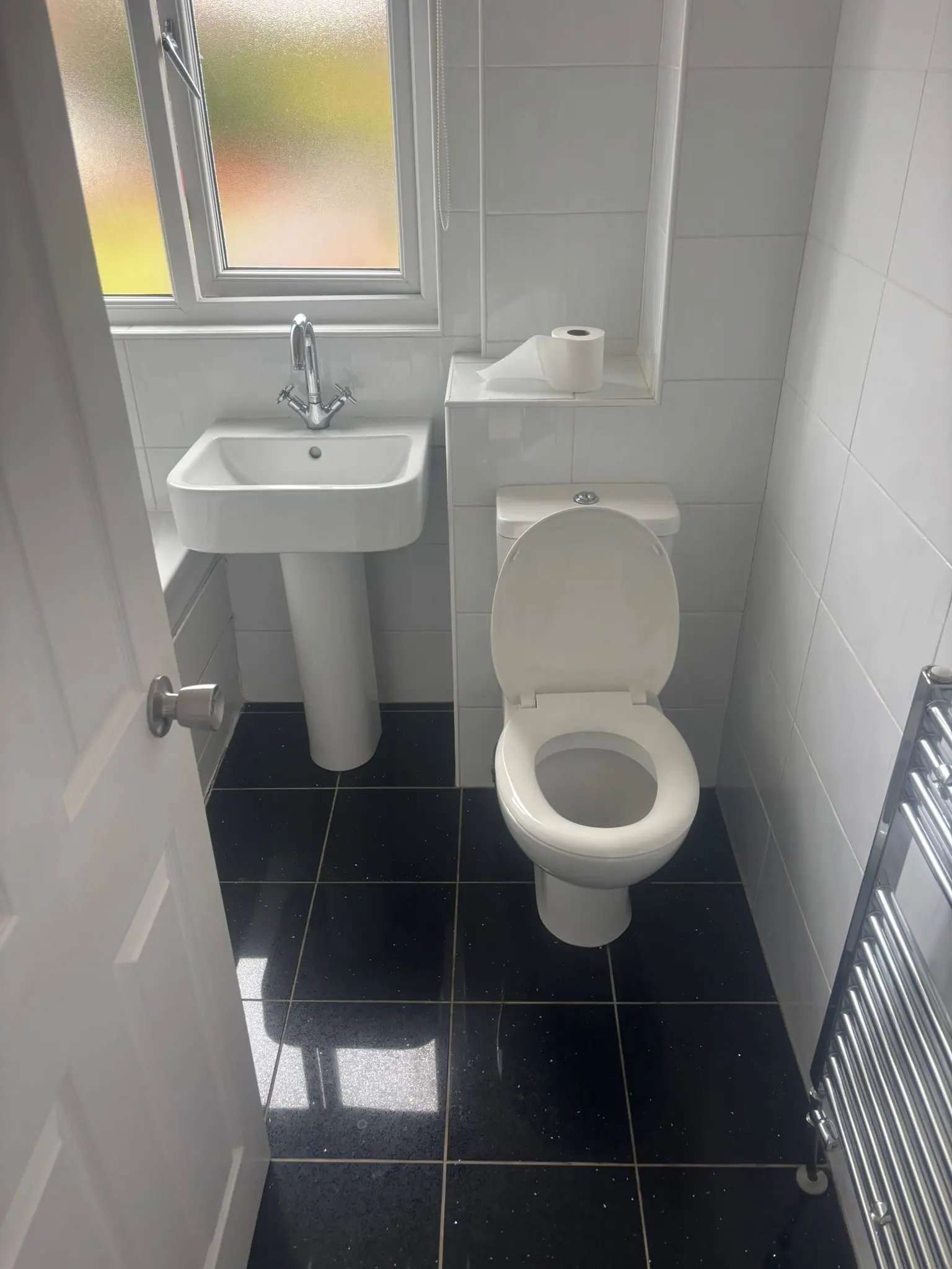 Dated pedestal basin and WC with black floor tiles before renovation