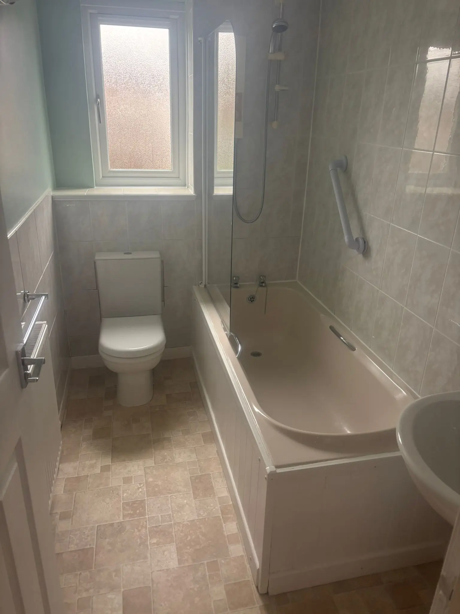 Dated bathroom with old bathtub, worn vinyl flooring and faded tiles before renovation in Stockbridge